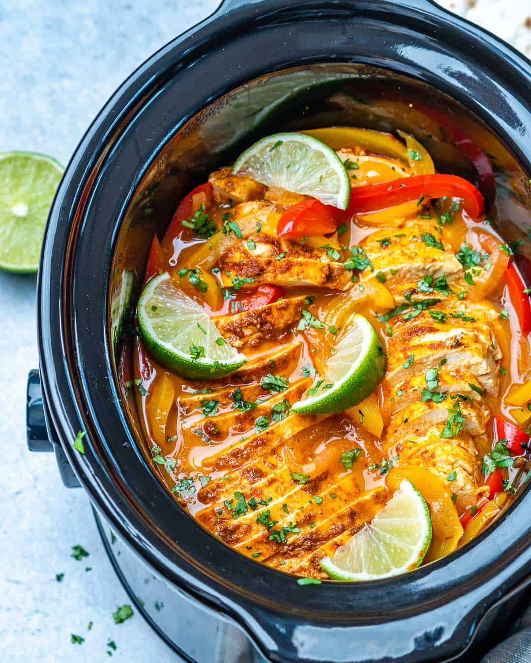 Slow cooker chicken fajitas in black Crockpot with limes and cilantro garnishes.