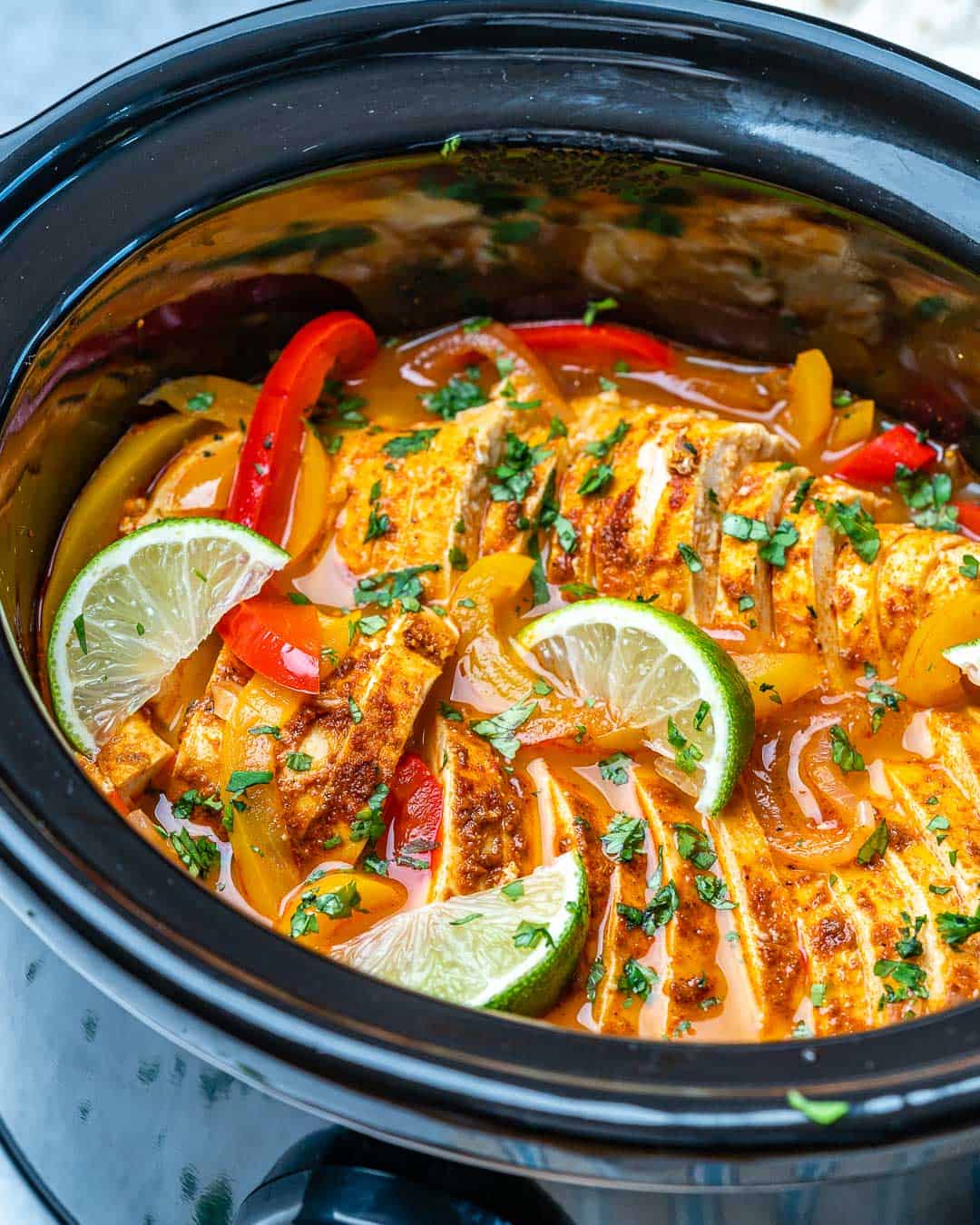 Crockpot with finished chicken fajitas garnished with lime and cilantro.