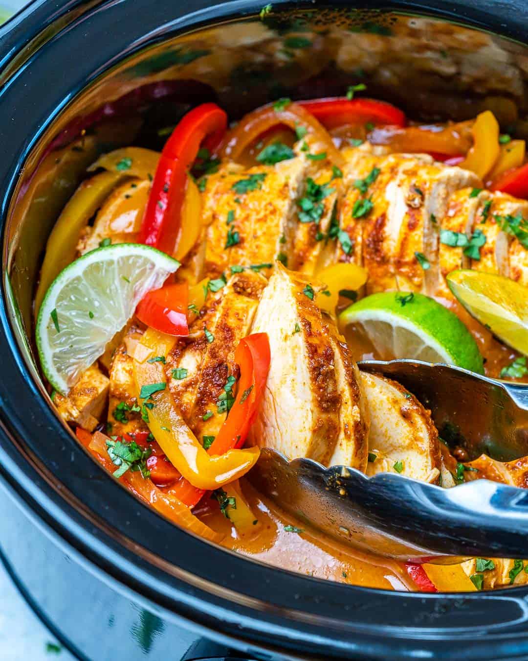 Tongs removing sliced chicken fajitas from black Crockpot. 