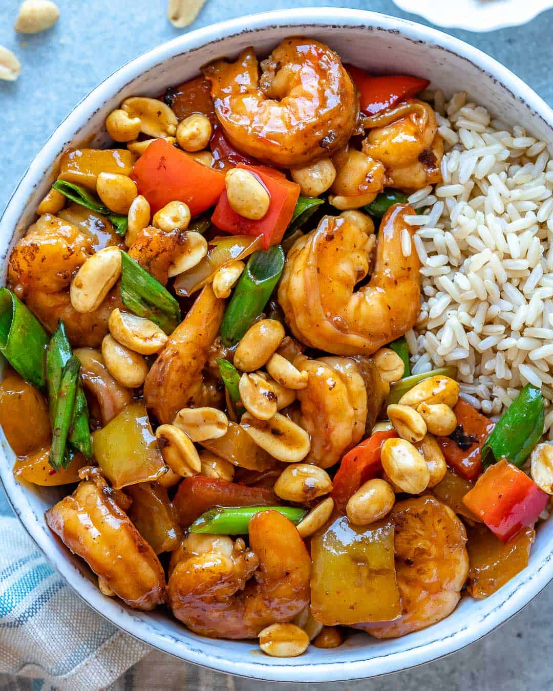 top view of kung pao shrimp in white bowl with brown rice
