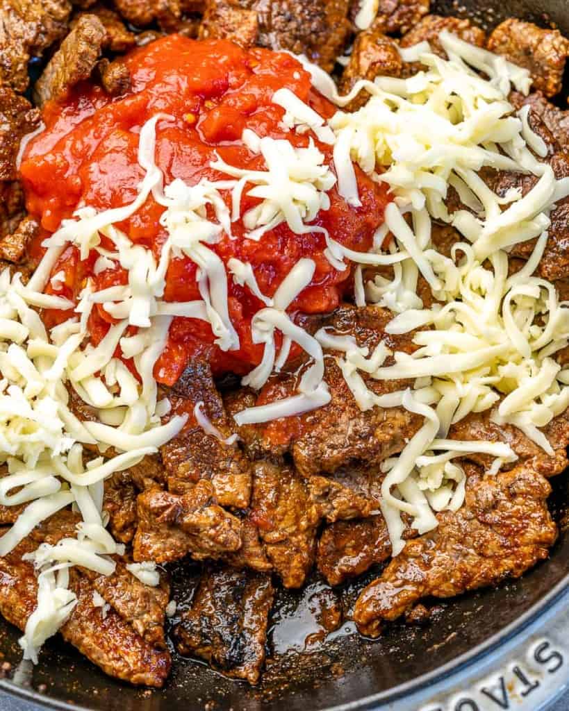 Overhead view of steak, shredded cheese and diced tomatoes in a skillet. 