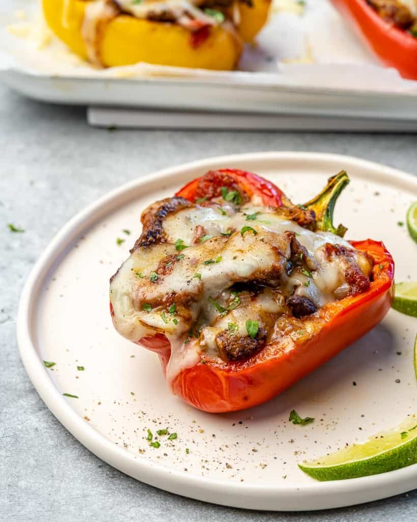 A red stuffed pepper on a plate with a wedge of lime. 