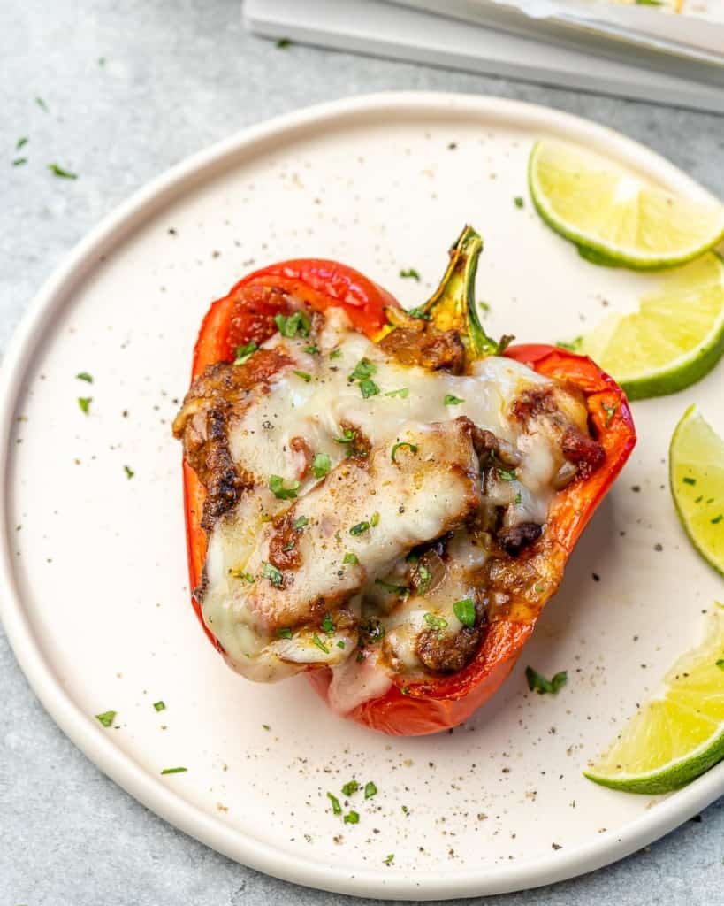 Overhead view of a stuffed pepper on aplte with lime wedges on the side. 