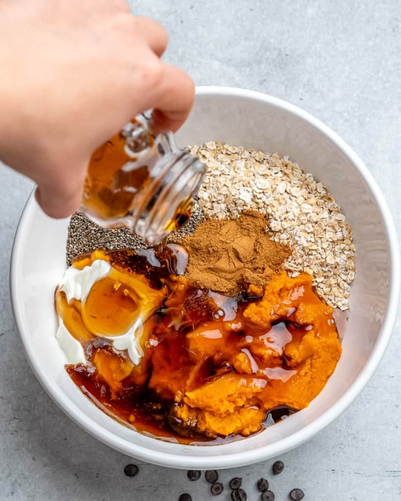 pouring maple syrup in a bowl with ingredients for pumpkin overnight oats 