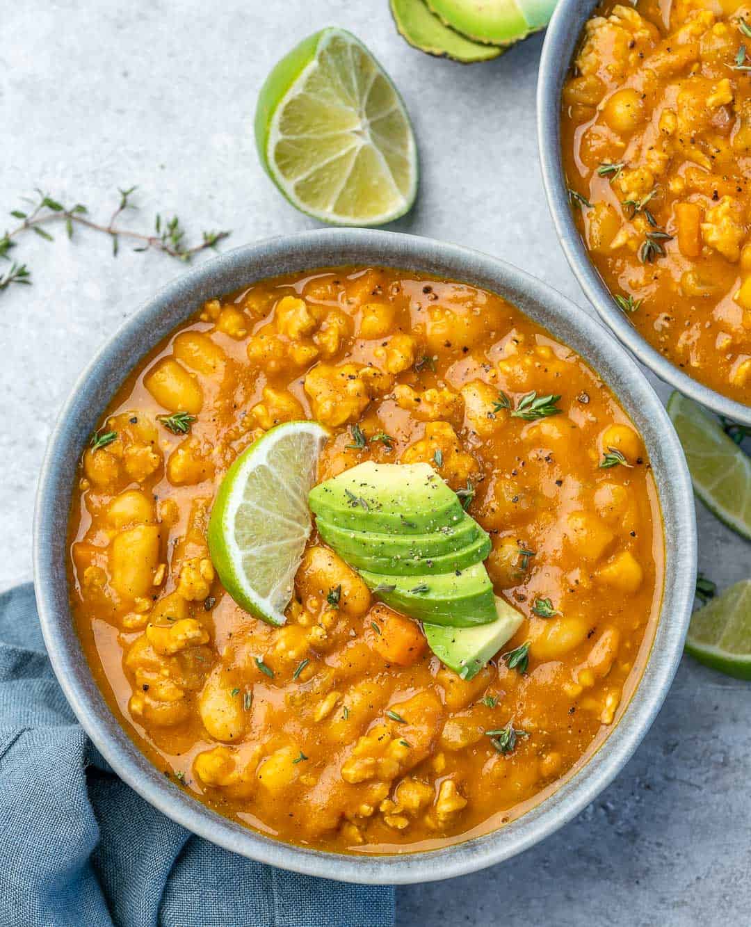 Two bowls of white bean turkey pumpkin chili with avocado slices on top