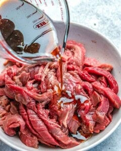 pouring sauce over the beef to be marinated.