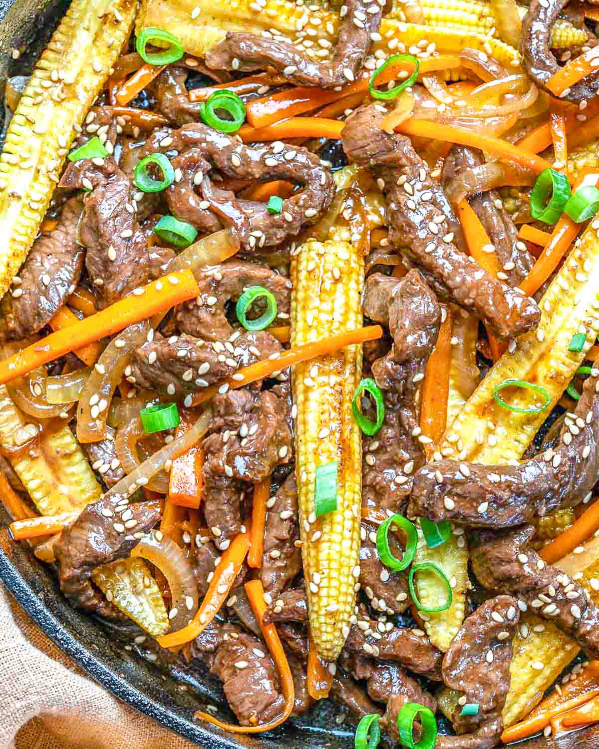 Beef stir fry with veggies in a black skillet.