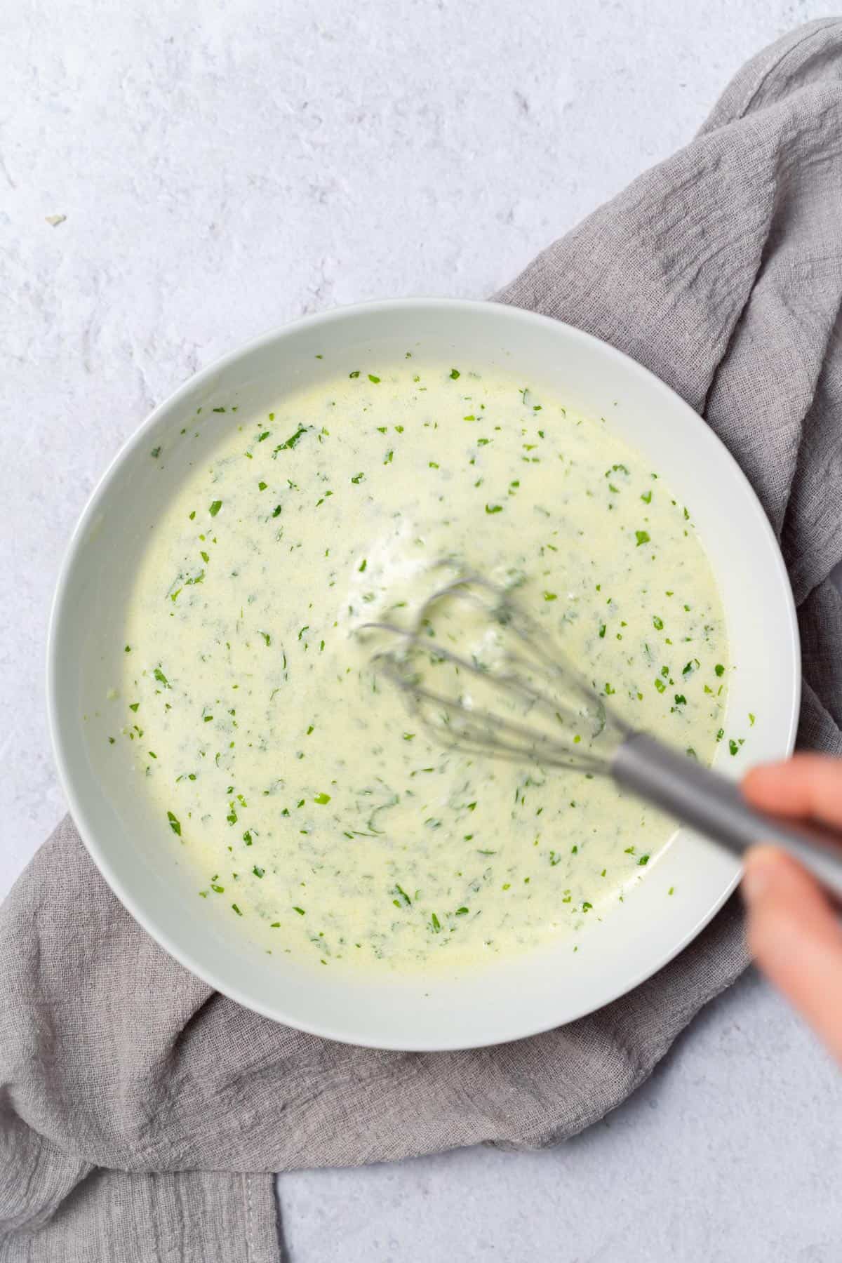 Whisking a creamy dressing in a white bowl.