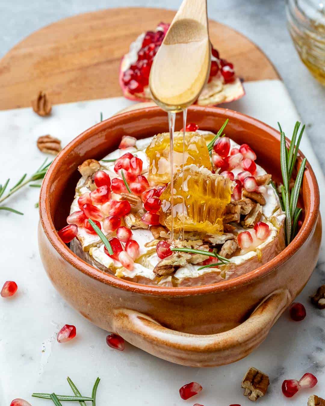 Drizzling honey on baked brie cheese with pomegranates and pecans