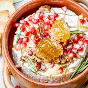 top view of baked brie in brown dish topped with honey and pomegranate