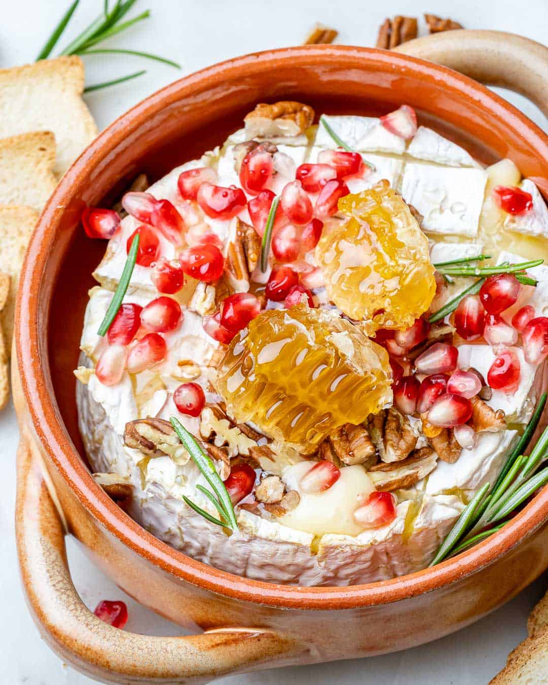 top view of baked brie in brown dish topped with honey and pomegranate
