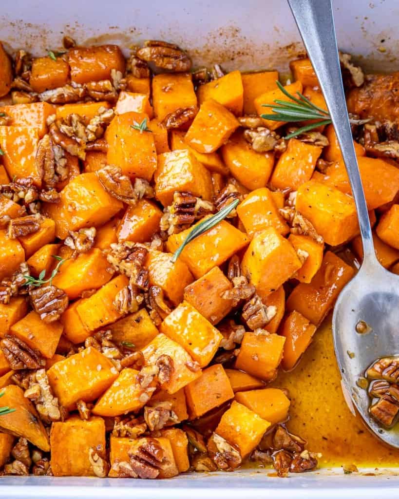 Overhead shot of maple roasted sweet potatoes in a white baking dish with a silver spoon.