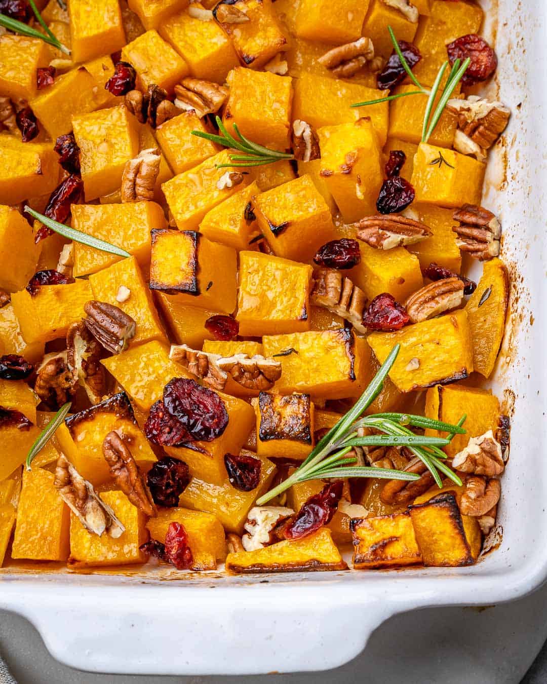 Top view of white baking dish with roasted butternut squash, pecans, and cranberries