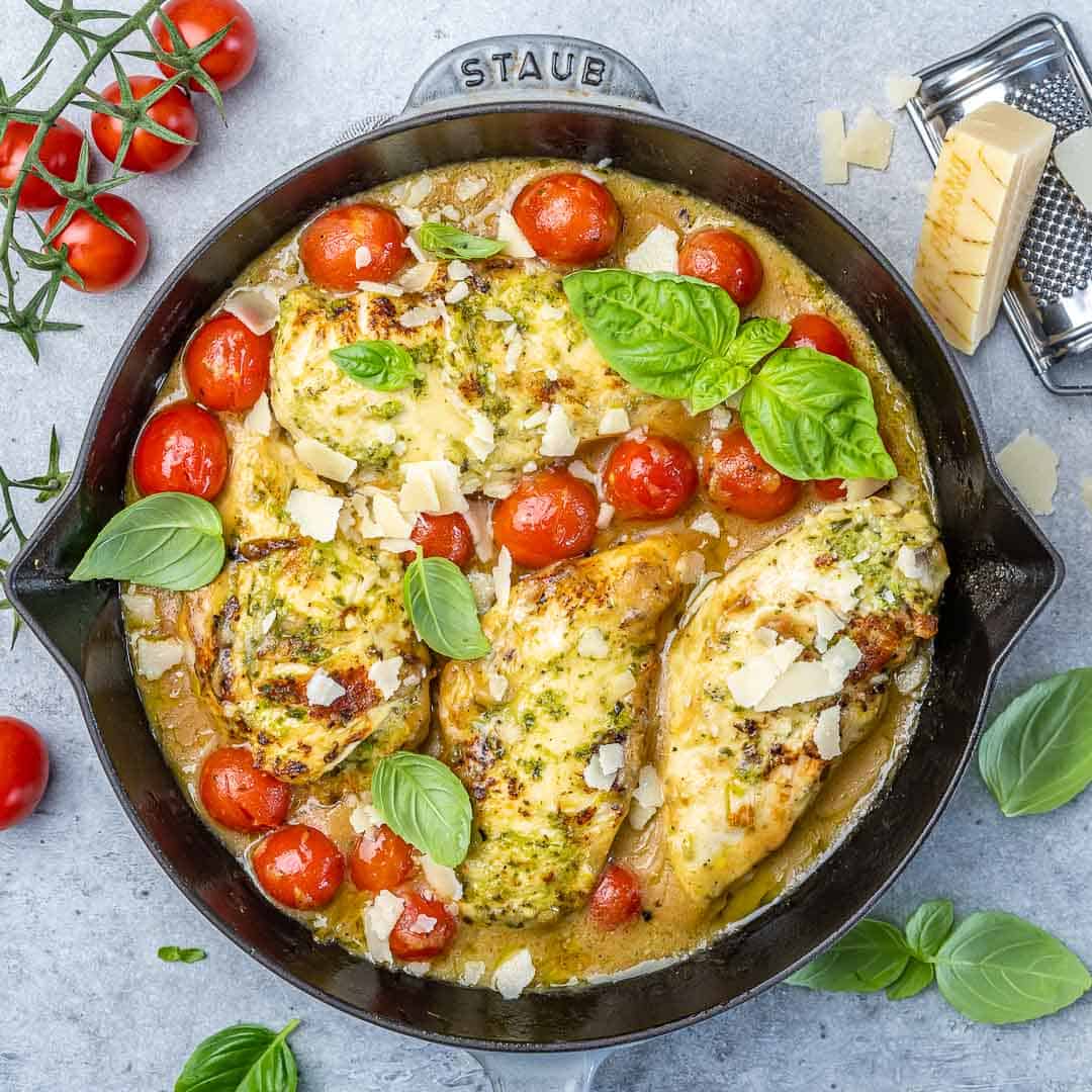 top view of pesto chicken and tomatoes in a black skillet with basil garnished