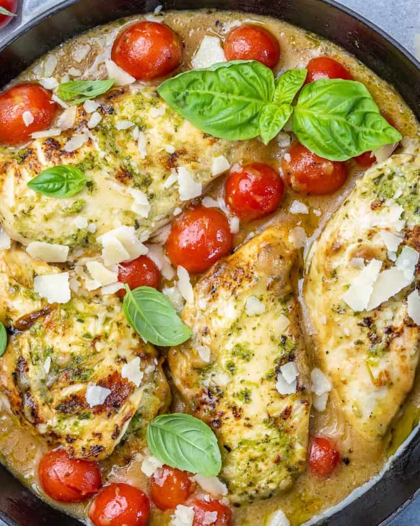 top view close up image of chicken breasts in pesto sauce and cherry tomatoes 