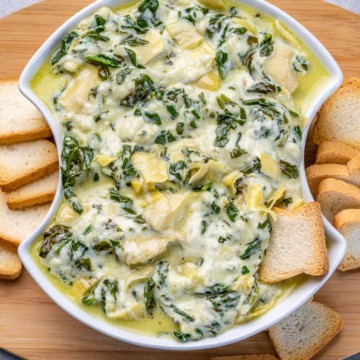 top view of spinach dip in a white bowl with slices of bread on the side