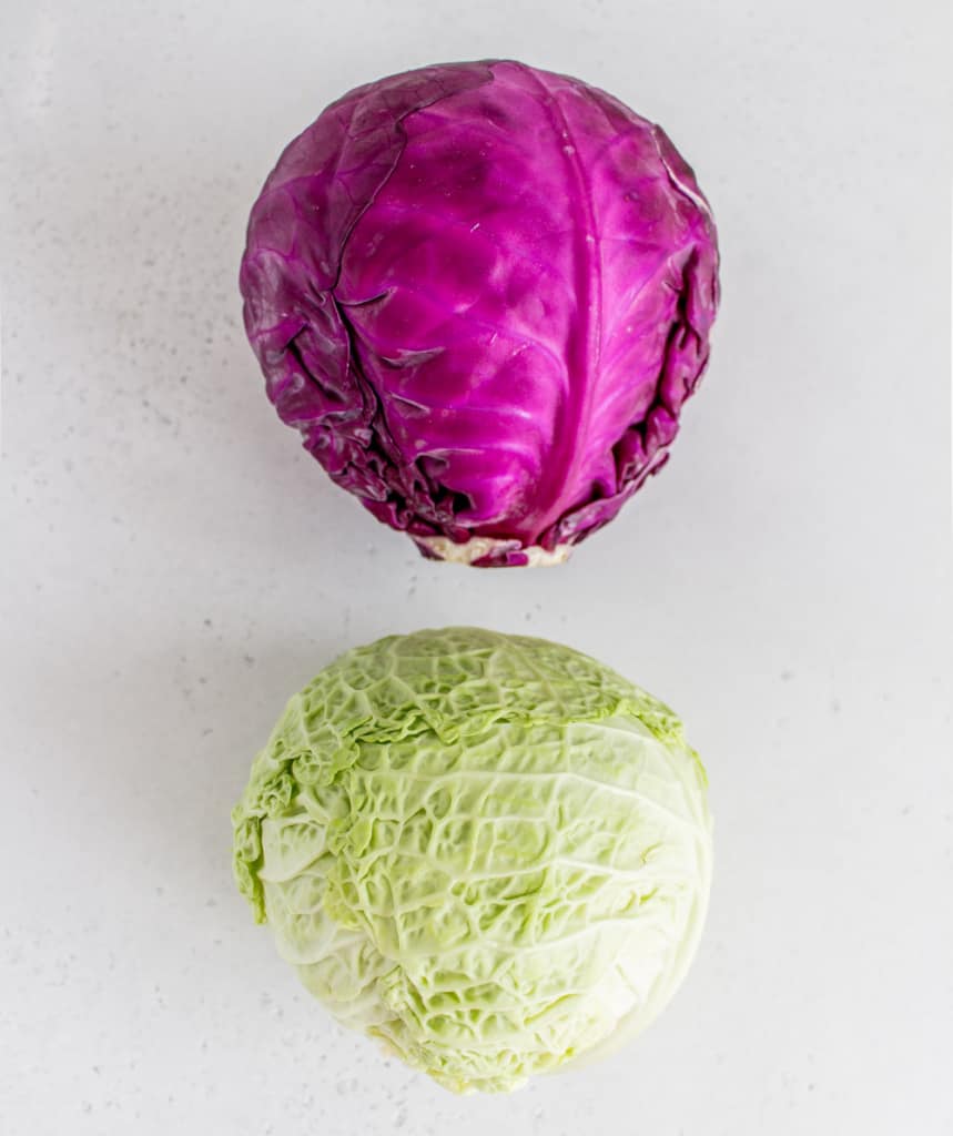 top view of two whole cabbage. One purple and one green 