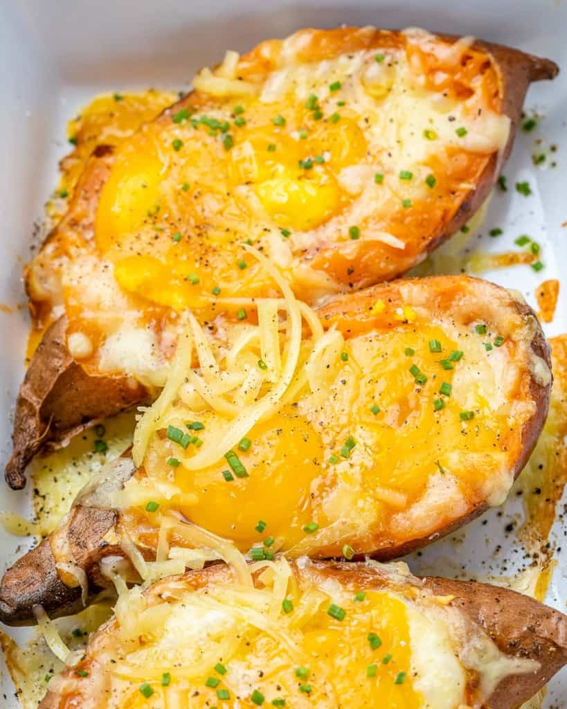 Three baked sweet potatoes in a white baking dish topped with melted cheese