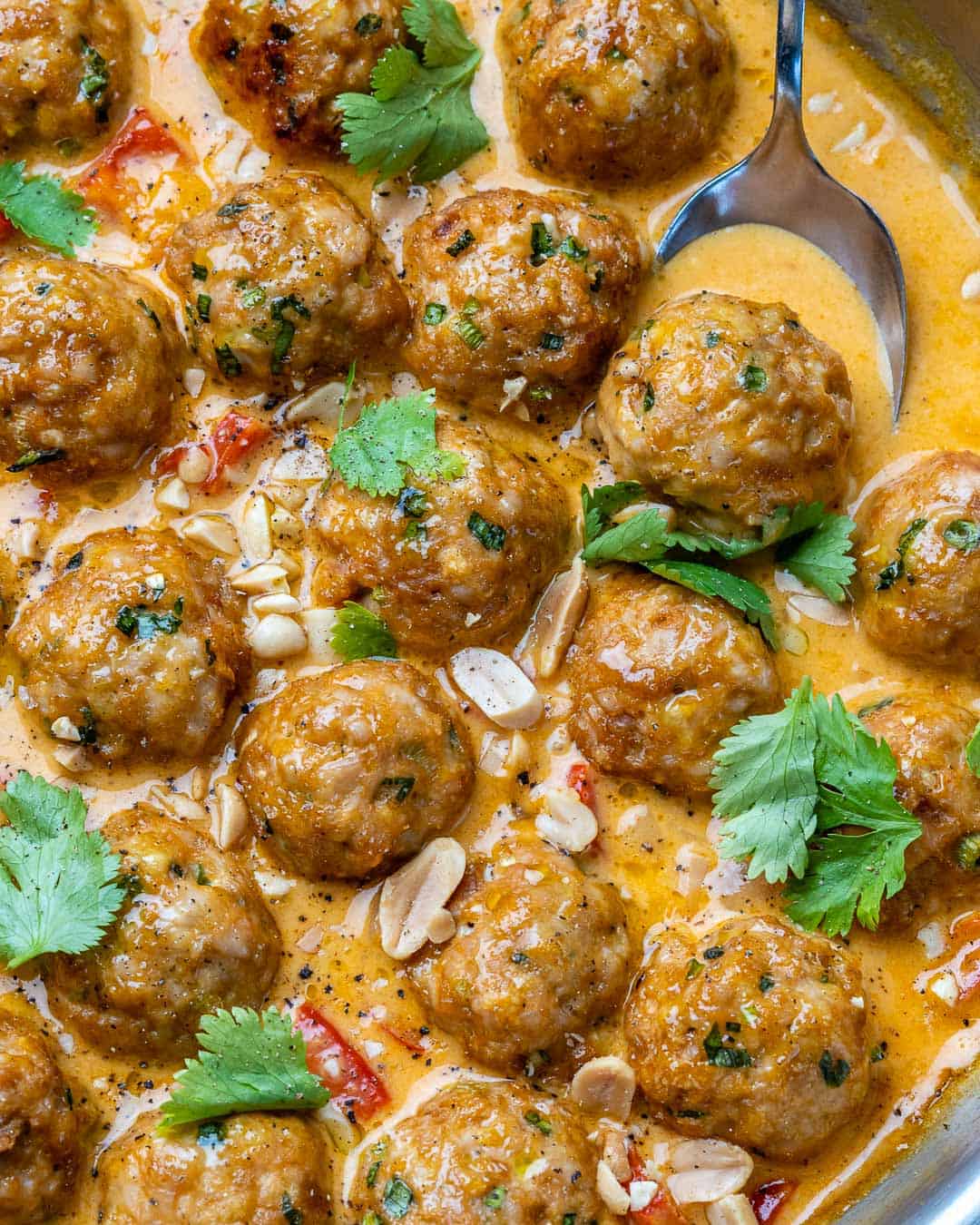 Spoon scooping out meatball in curry sauce garnished with cilantro and peanuts. 