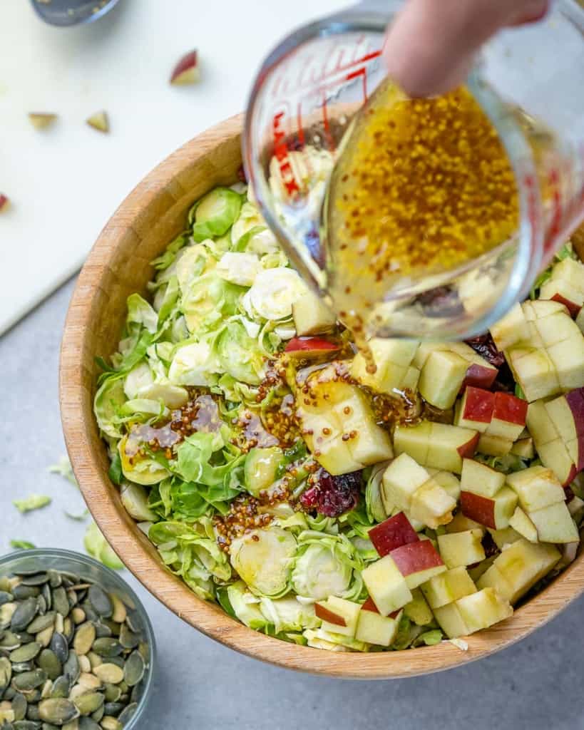 Salad dressing being poured onto a bowl of salad.