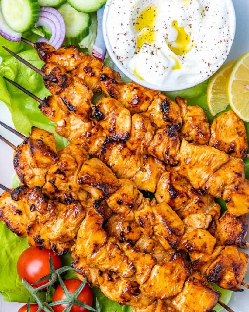 top view chicken skewers on a plate with a side of yogurt garlic dip