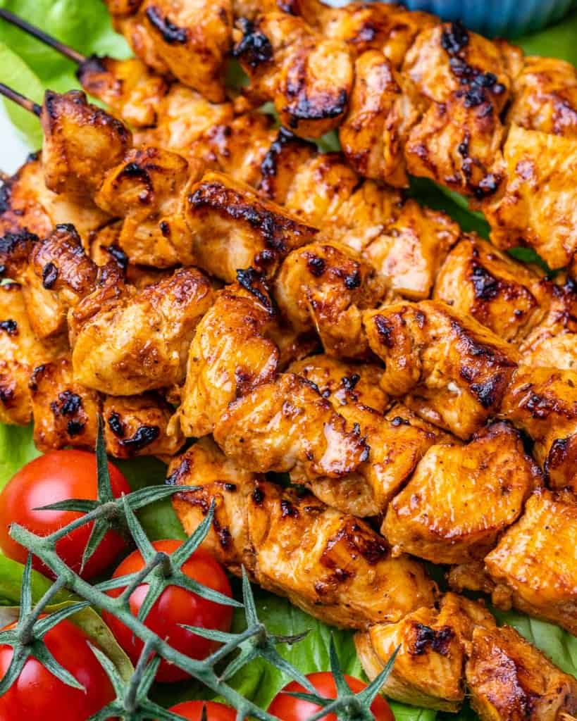close up image of grilled chicken tawook kebabs on a bed of lettuce next to cherry tomatoes as garnish