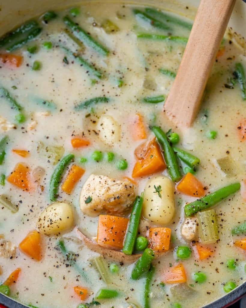 Close up of a pot of soup with gnocchi and vegetables.
