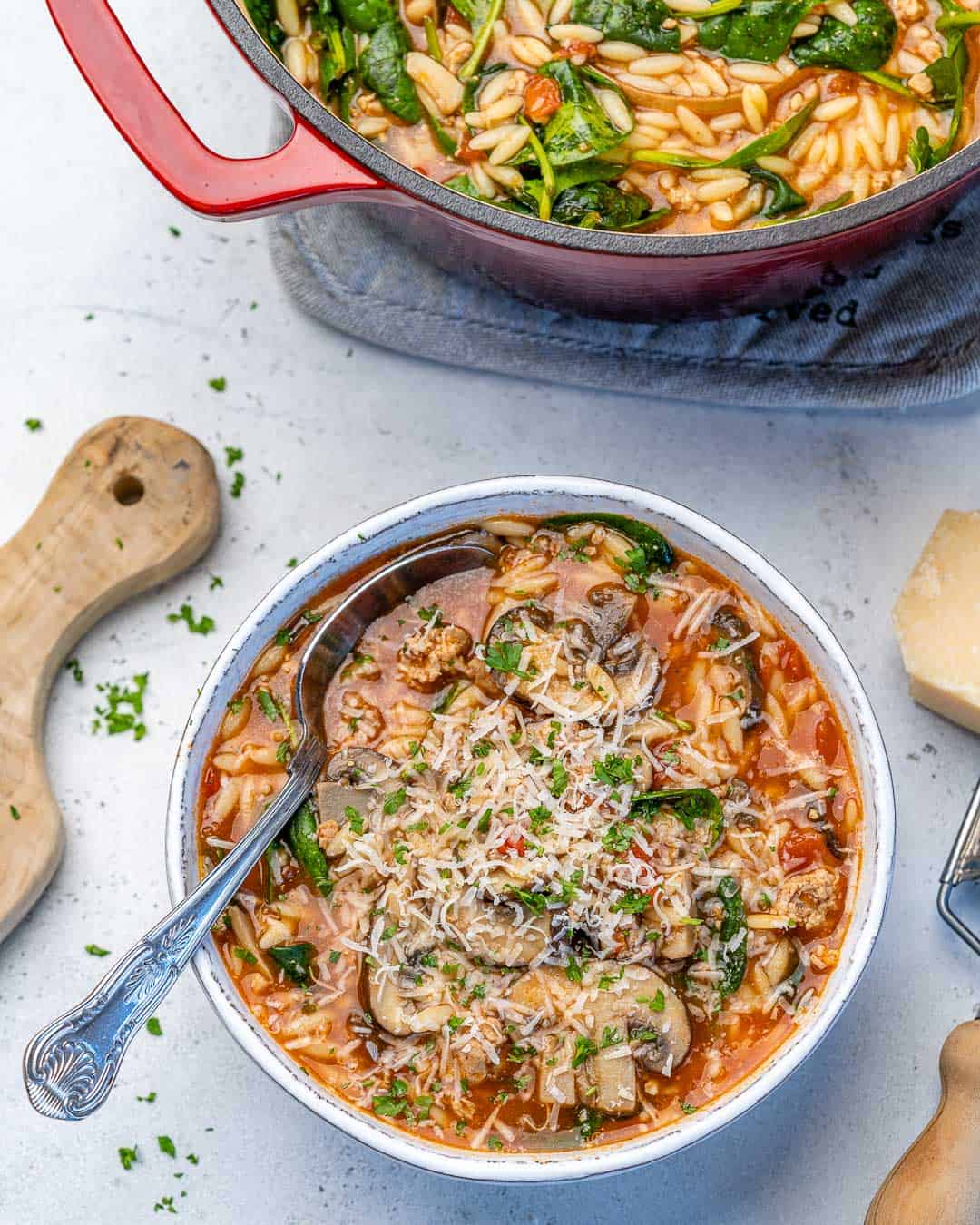 one bowl of chicken orzo soup with spinach and a spoon topped with cheese