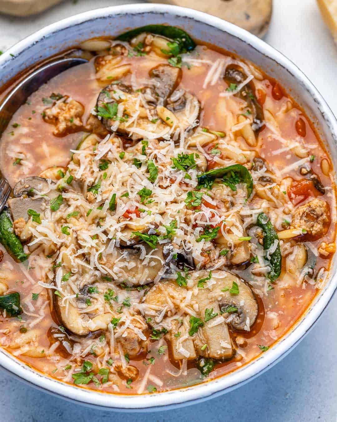 close view of chicken orzo soup in a bowl with spinach, cheese, and mushrooms