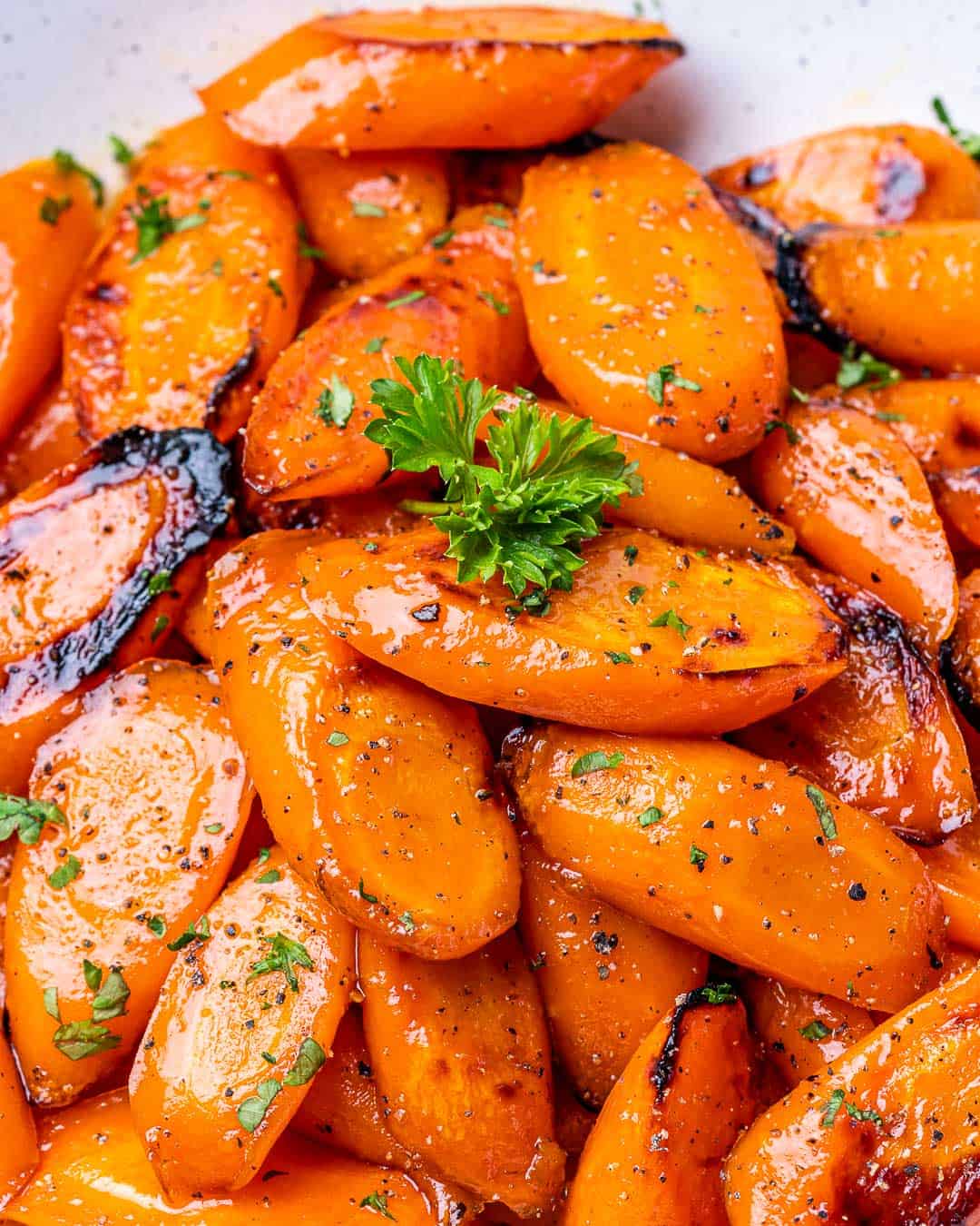 Close view of roasted honey glazed carrots in a bowl with parsley garnish