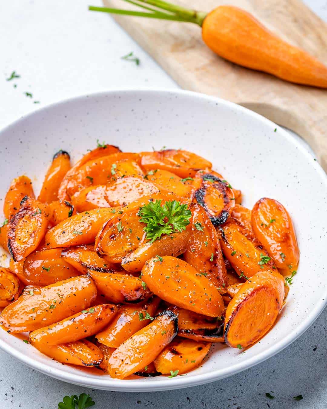 White bowl with roasted honey glazed carrots and whole carrot in background