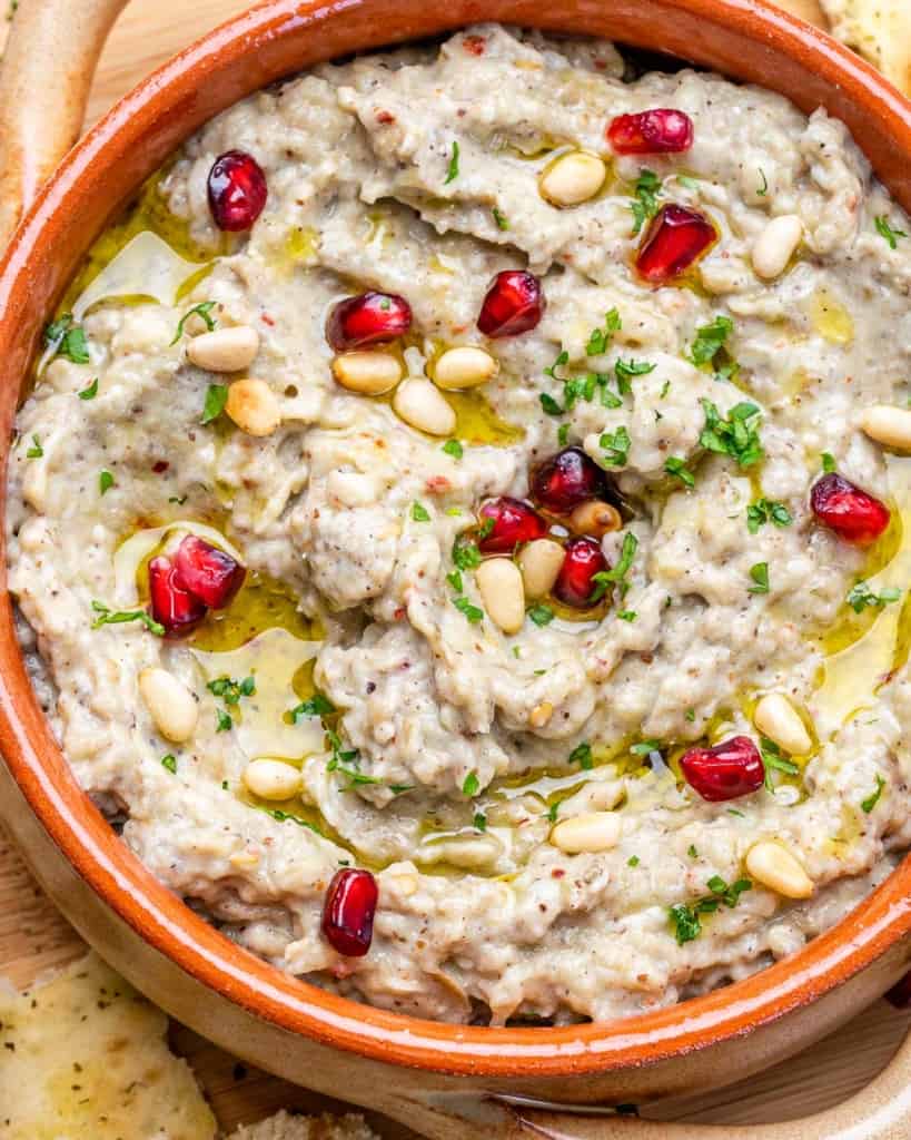 close up baba ganoush in a bowl with parsley and pine nuts garnishes