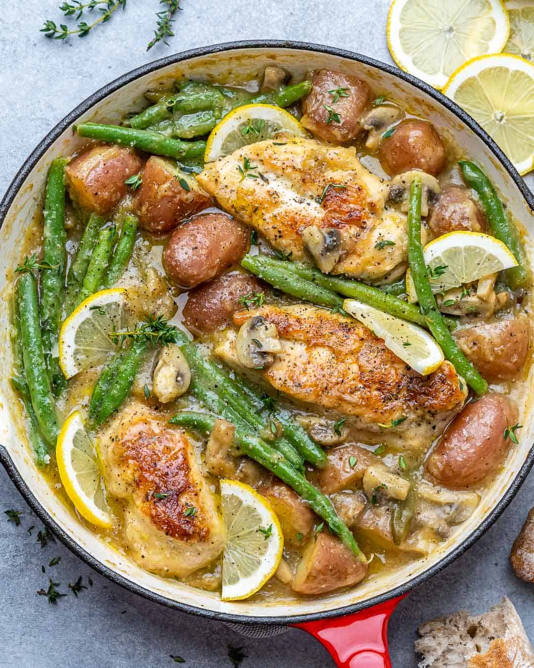 top view chicken skillet with potatoes and green beans topped with lemon garnishes