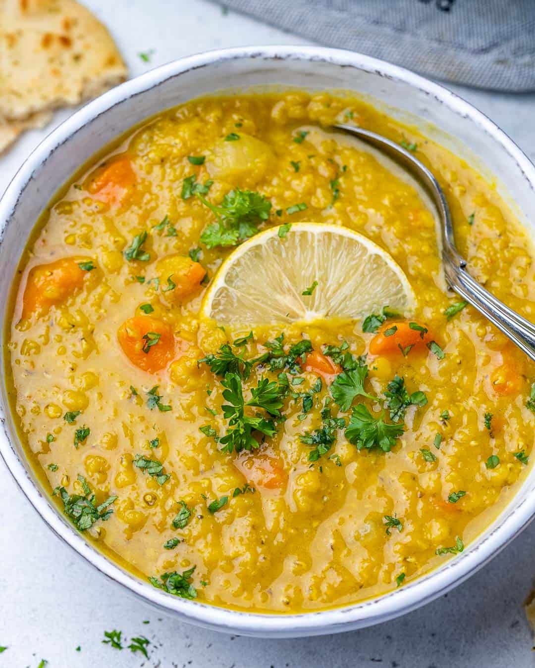 top view lentil soup in white bowl with spoon in it and lemon slice garnish