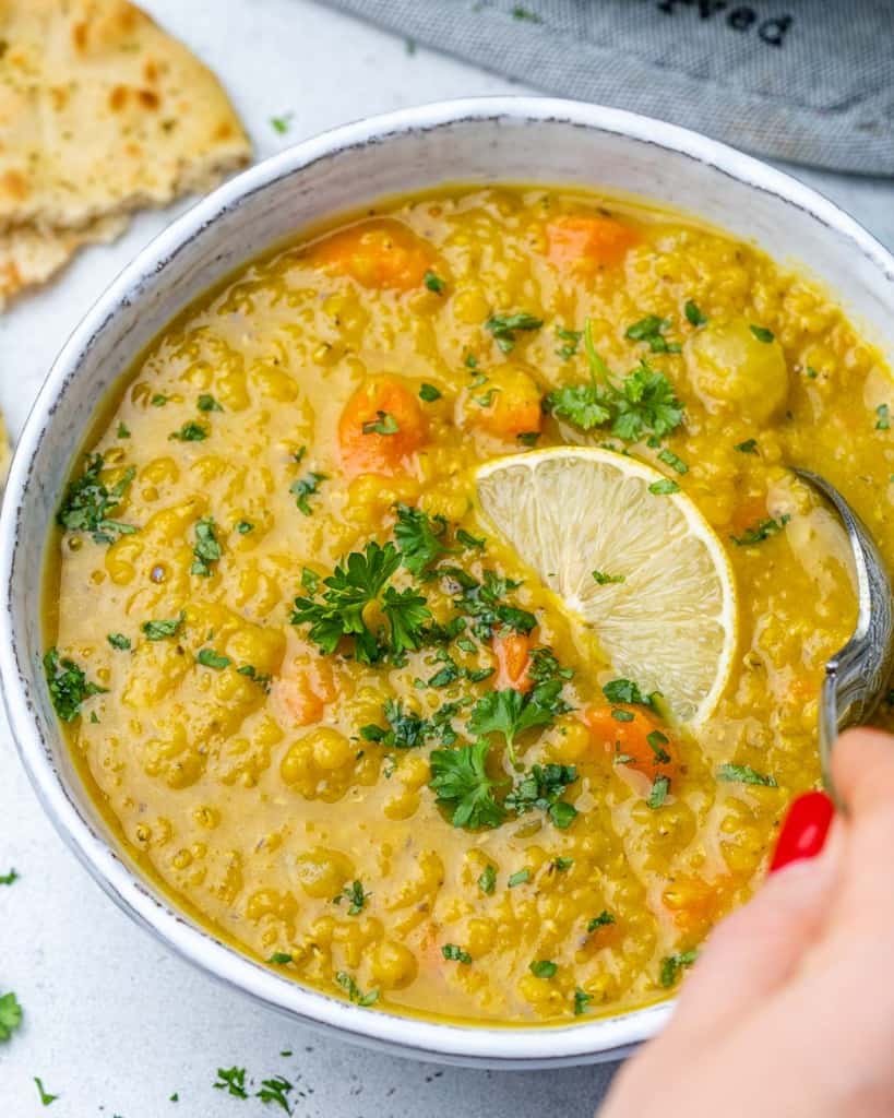 top view of lentil soup in white bowl with hand holding spoon