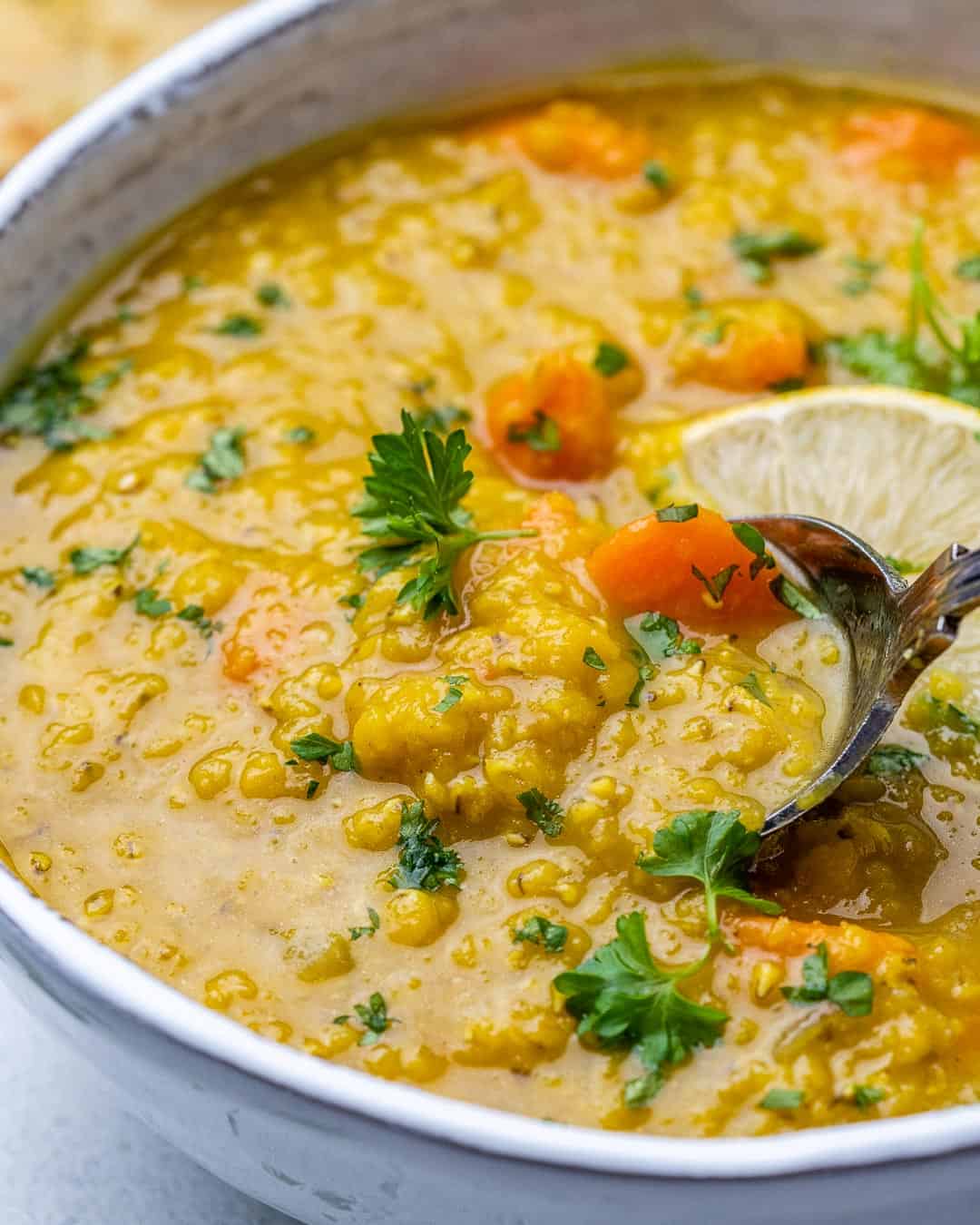 Spoon scooping vegan red lentil soup from bowl garnished with parsley