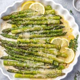top view of baked asparagus in a white dish with lemon garnishes