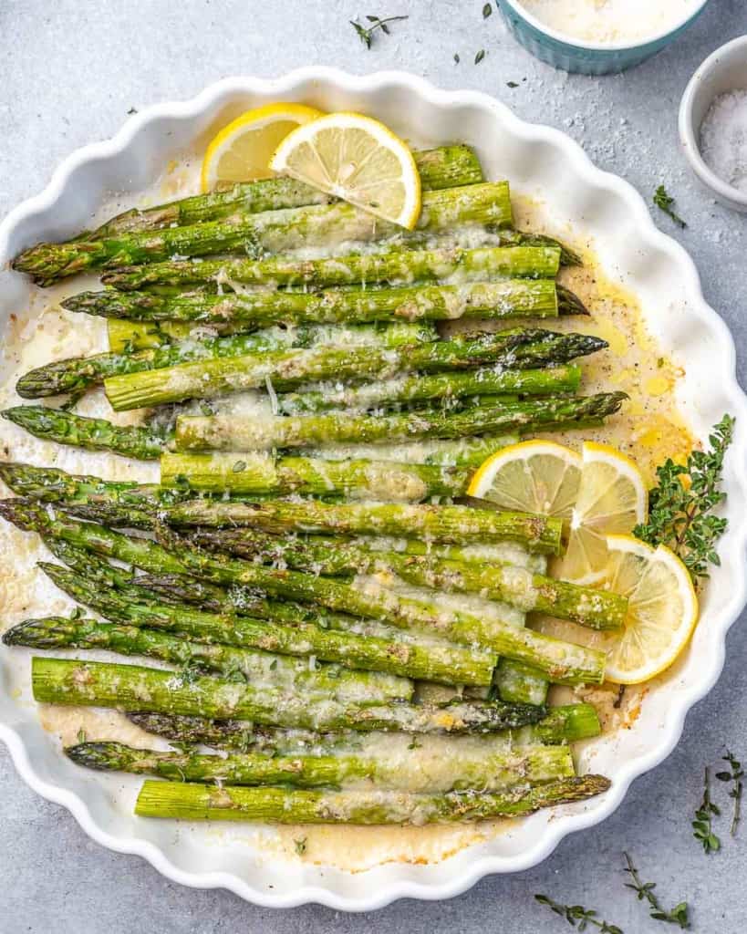top view of baked asparagus in a white dish with lemon garnishes