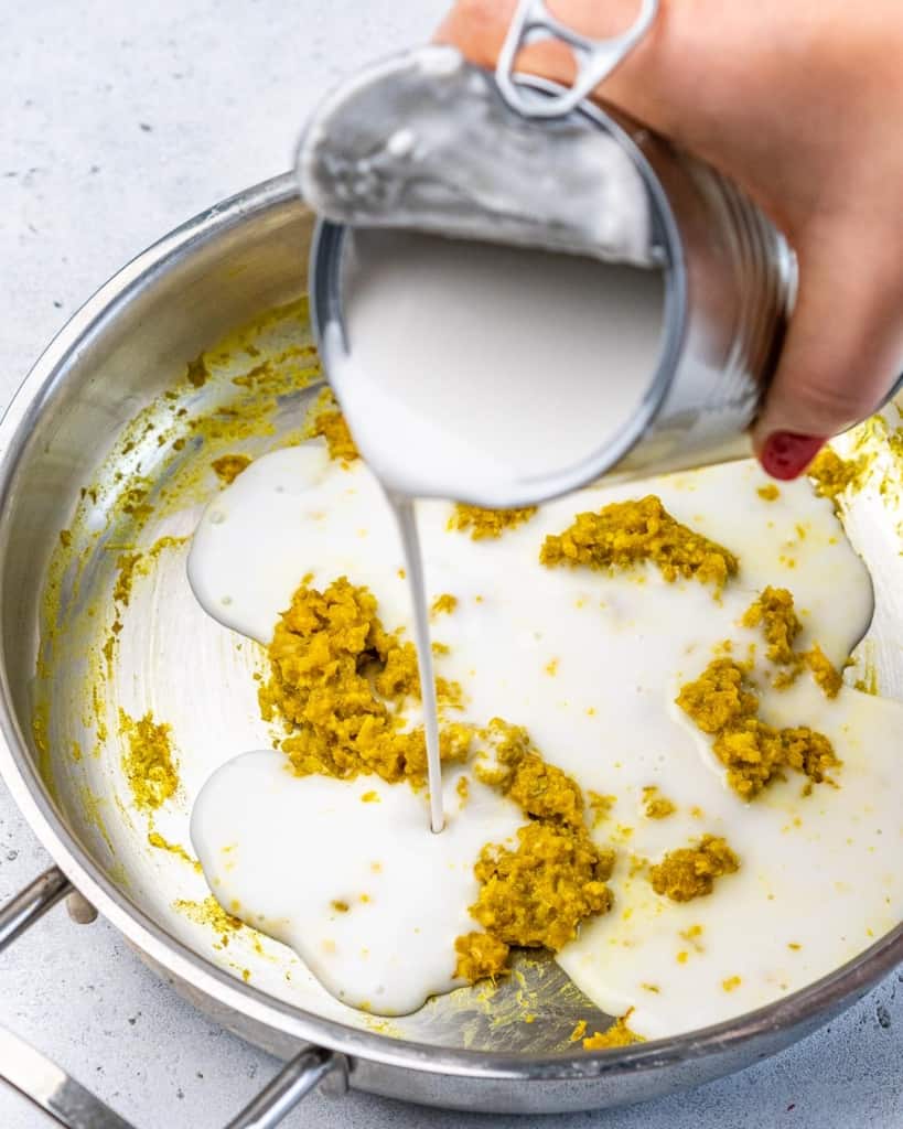 coconut milk being poured in a pan of curry paste 