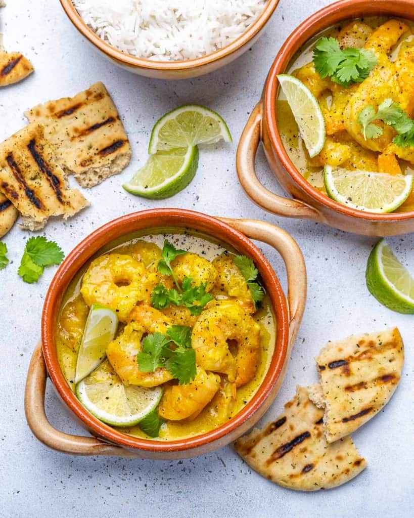 top view of two bowls of shrimp curry with lemon and cilantro garnishes