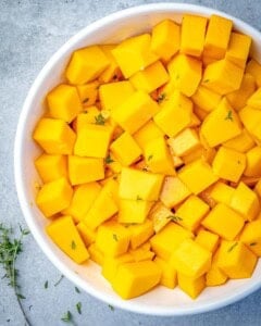 a bowl with butternut squash coated in maple syrup mixture.