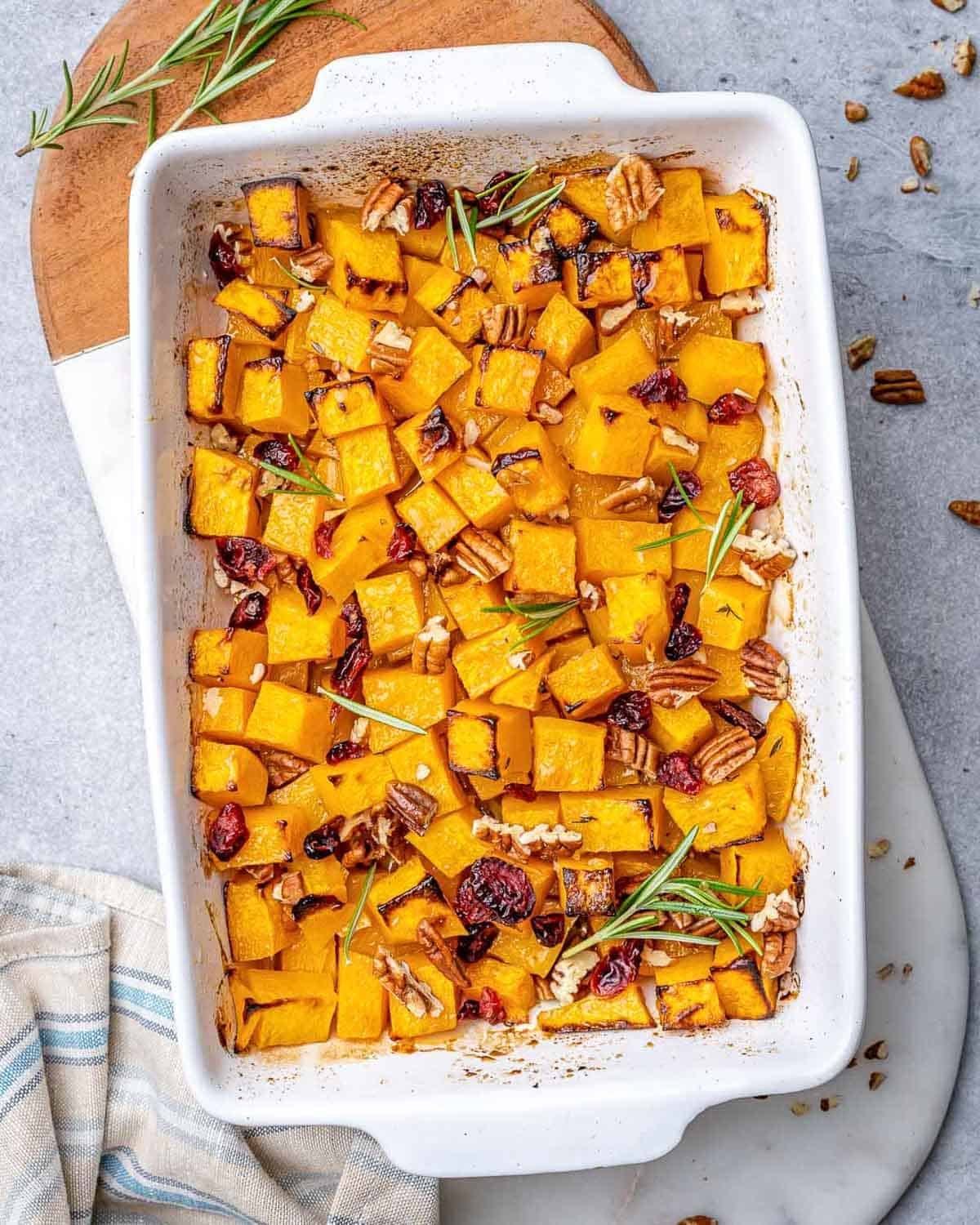 maple roasted butternut squash in a dish with fresh thyme, cranberries, and pecans.