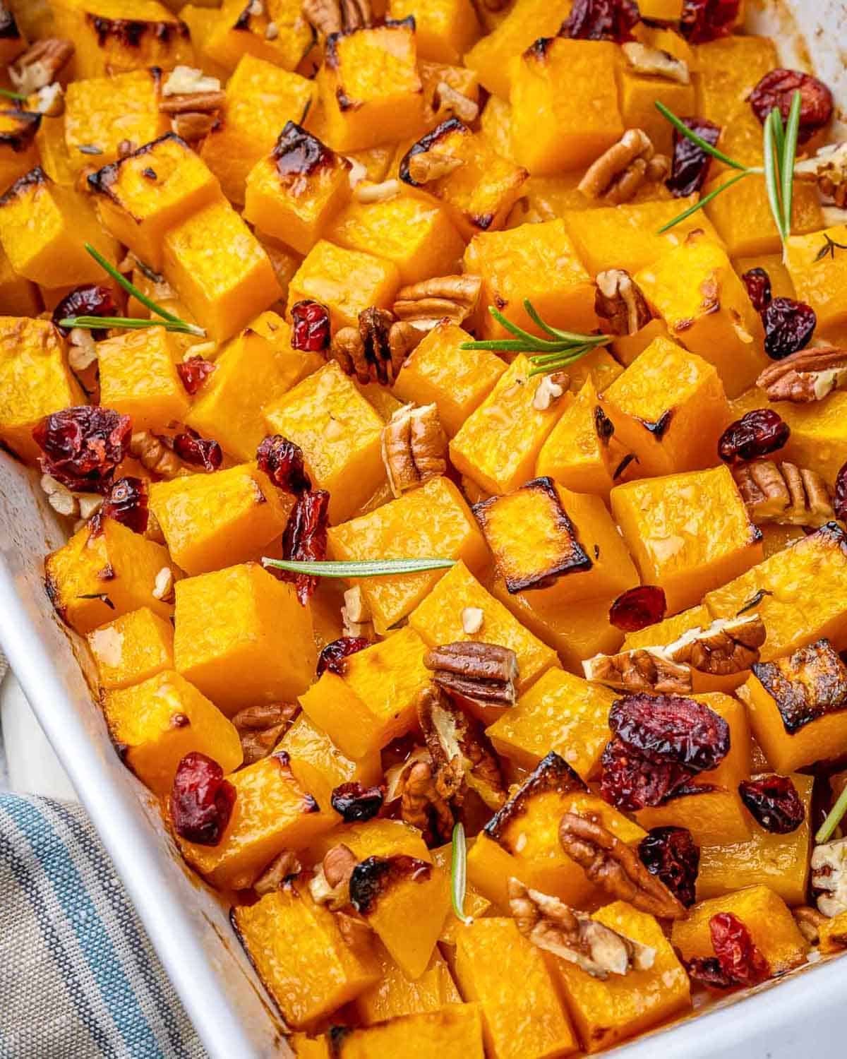 roasted butternut squash squares in a dish with pecans and dried cranberries.