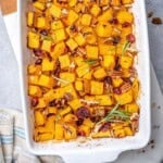 a baking dish with roasted butternut squash squares topped with pecans and cranberries.