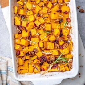 a baking dish with roasted butternut squash squares topped with pecans and cranberries.