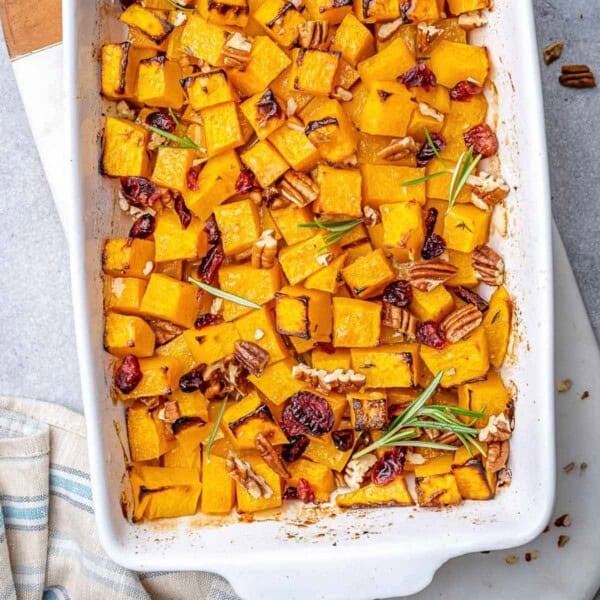a baking dish with roasted butternut squash squares topped with pecans and cranberries.