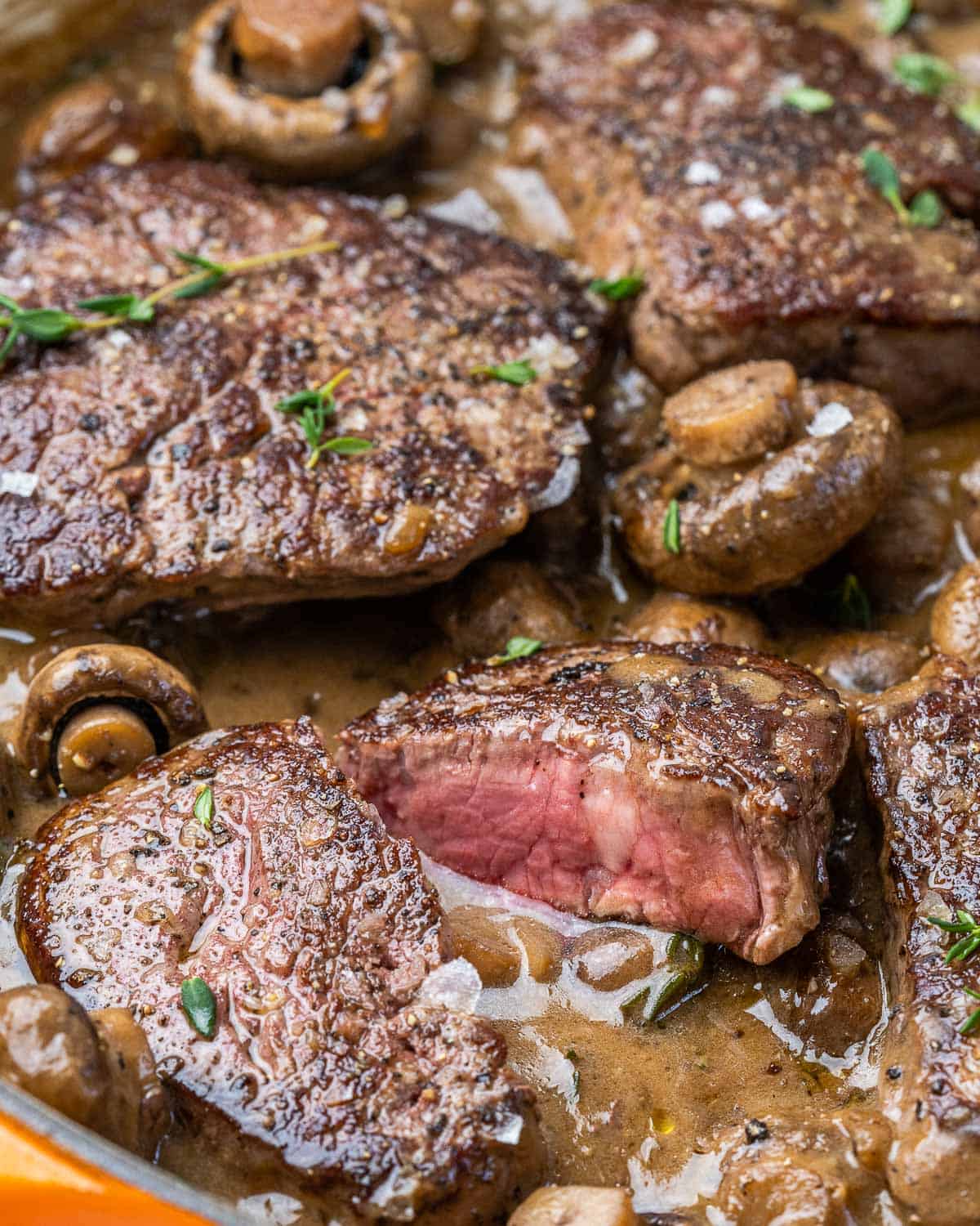 Filet mignon steak cut open in skillet with mushroom sauce. 