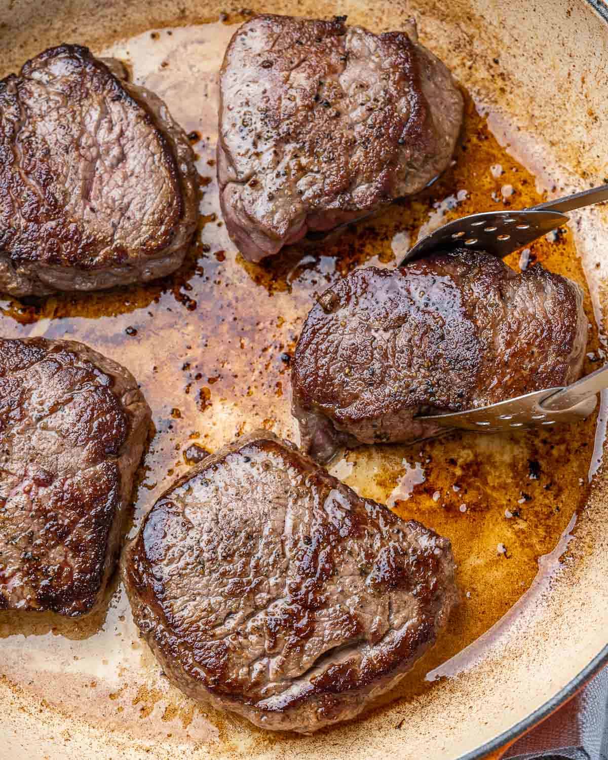Tongs removing seared steak from pan.