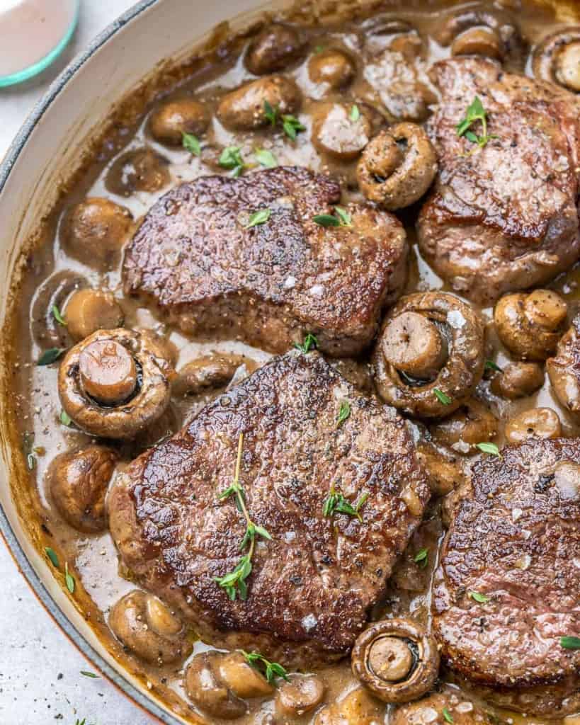 top view steak in a creamy mushroom sauce in a yellow skillet