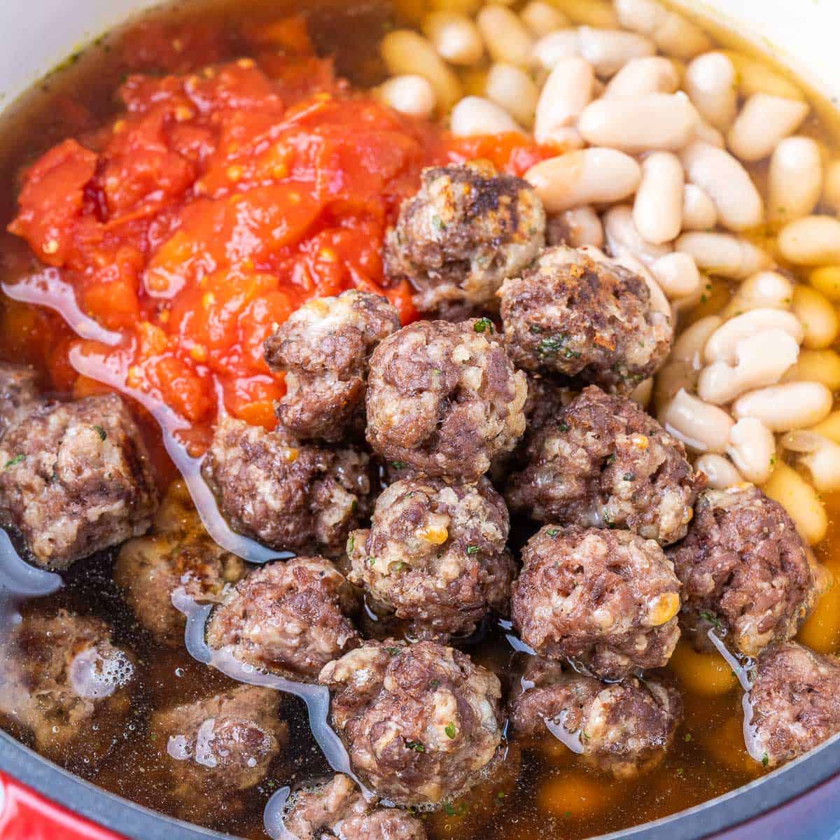 Adding cooked meatballs to pot of soup.